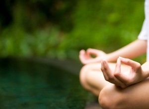 Woman sitting in the grass doing a yoga hand pose.
