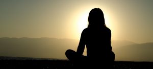 Silhouette of a woman sitting and observing a yellow sunset.